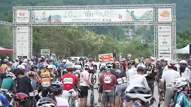 自行車騎士在南庄活動拱門下集結，背景可見山林。