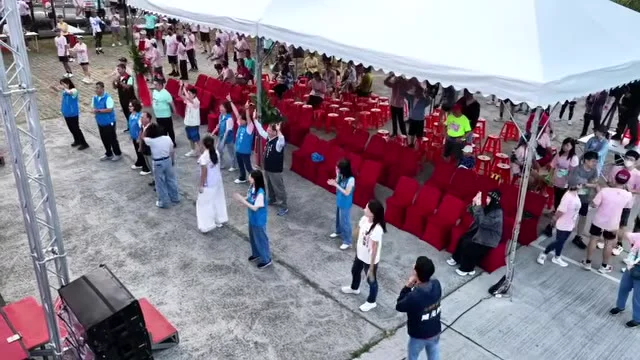 活動帳篷內排列紅色座椅，多位參與者與現場人員在典禮區相聚。