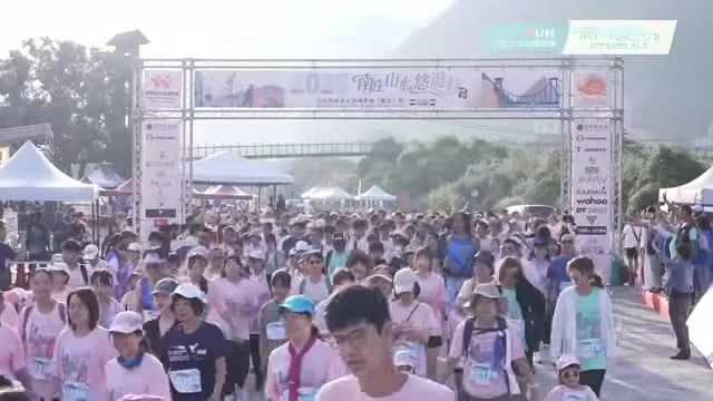 畫面中跑者沿停車場旁道路前進，遠處可見拱門與山景。